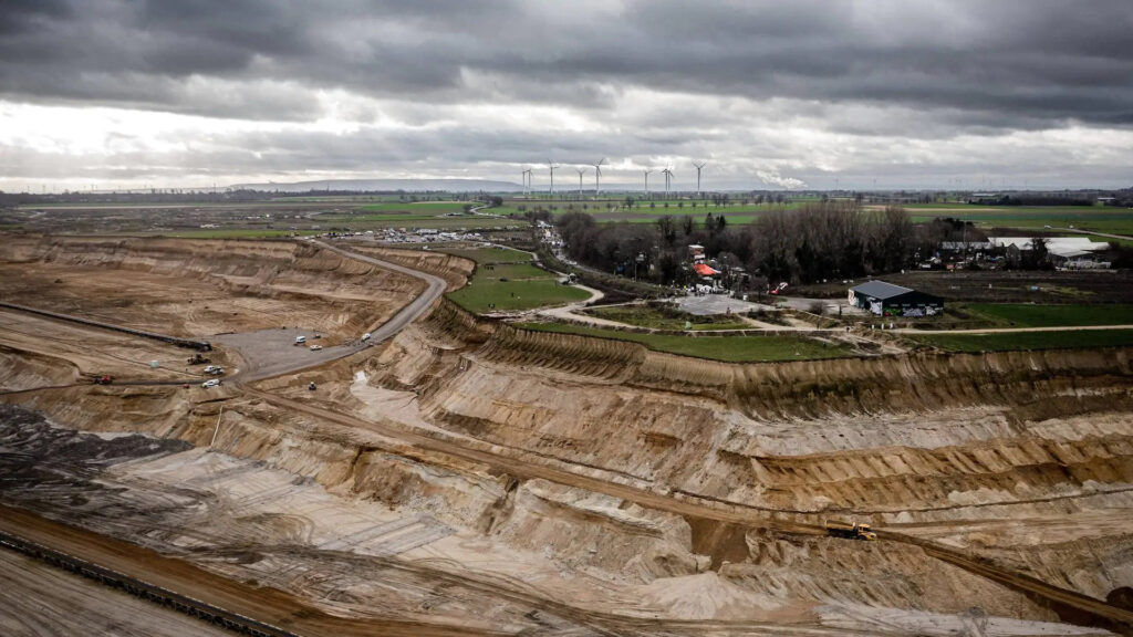 The village of Lüetzerath, among woods and farms, standing at the edge of a cliff as if an island over nothing.  All around it, the enourmous crater of the coal mine.
