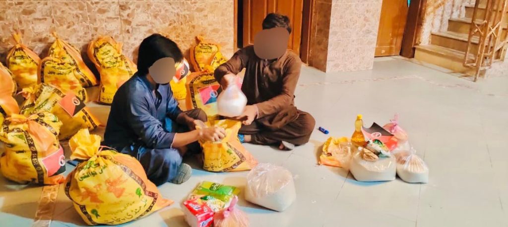 zwei Männer* sitzen am Boden und verpacken Lebensmittellieferungen in Plastiktüten