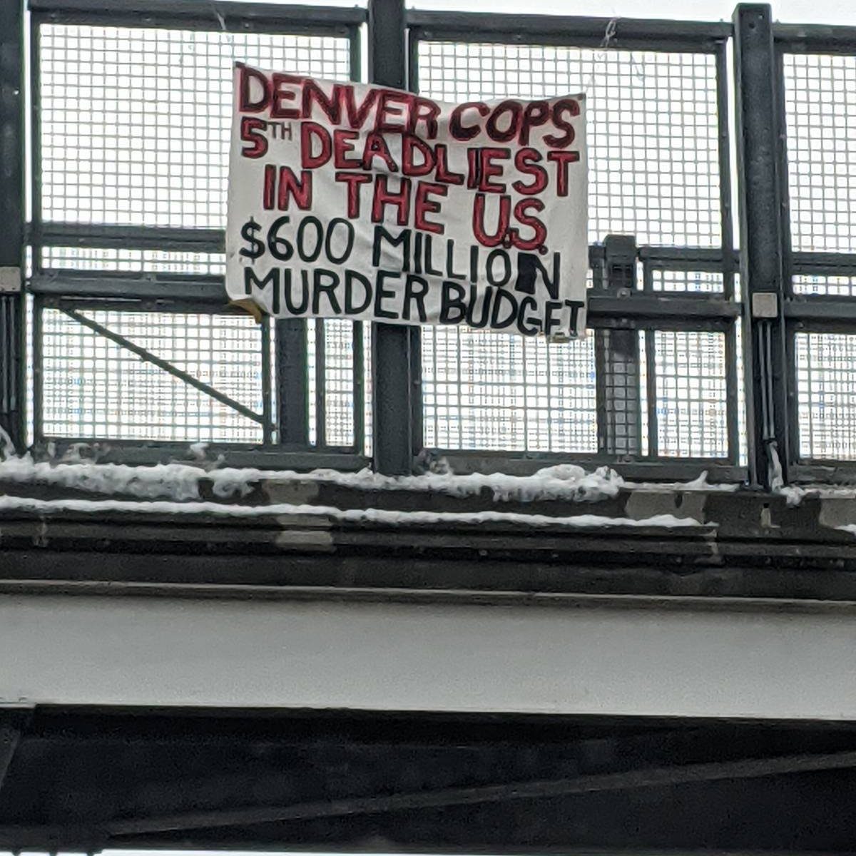 A banner hung over a bridge that reads "Denver Cops 5th deadliest in the US. $600 Million Murder Budget"