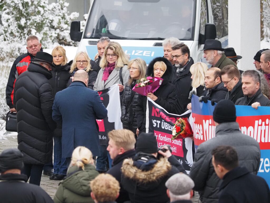 AfD-Kundgebung vor dem Illerkirchberger Rathaus. Menschen stehen mit Bannern und Blumen. 