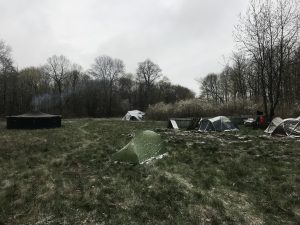 Eine leicht verschneite Wiese mit einem großen, schwarzen Rundzelt, aus dem der Rauch eines Feuers aufsteigt, und vielen kleineres Zelten, die von einer leichten Schneeschicht bedeckt sind. Es sieht kalt, aber auch irgendwie gemütlich aus.